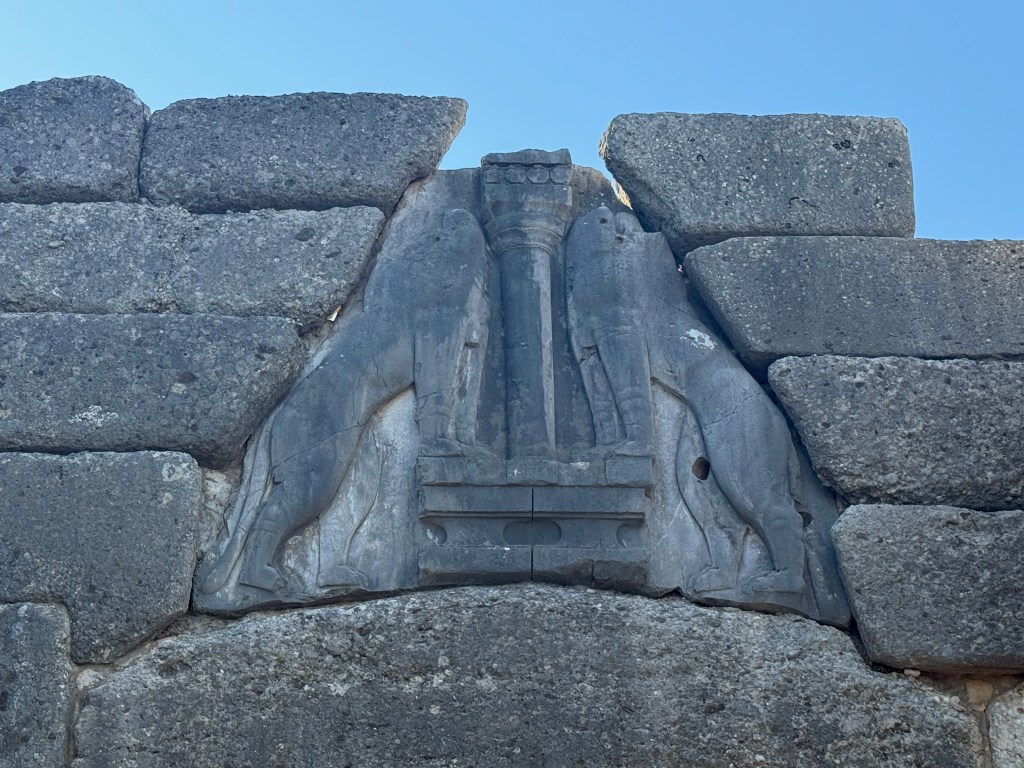 Relief sculpture of two lions flanking a central column, embedded in an ancient stone wall.